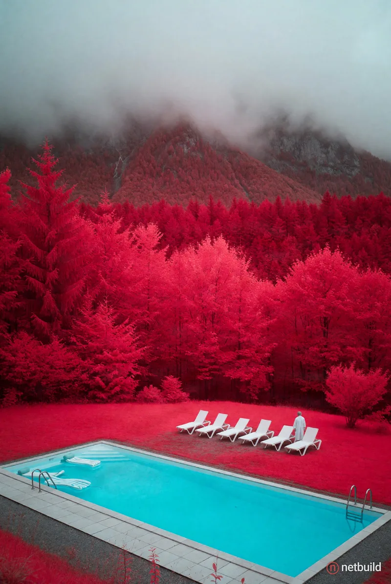 surreal infrared photography landscape, vivid turquoise rectangular swimming pool in the foreground, striking contrast against a dense crimson and bri...